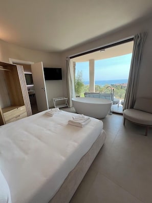 A hotel room with a large bed, a bathtub, a seating area, and a balcony with a view. - Il Nido Resort (Imperia)