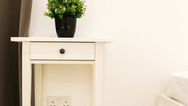 A white bedside table with a drawer, a shelf, and a potted plant. - Inhawi Hostel (St. Julian's)