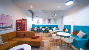 A modern lounge area with a blue sofa, orange couch, and white chairs. - Inhawi Hostel (St. Julian's)