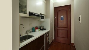 A compact kitchen with white cabinets, a stainless steel sink, a microwave, and a wooden door. - Istay Hotel Apartment 1 (Hanoi)