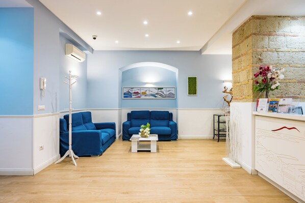 A room with two blue sofas, a white coffee table, a white reception desk, and a stone wall. - Residenza Matilde by NapoliApartments (Naples)