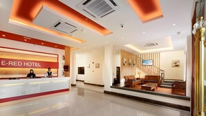 A hotel reception area with a modern design, a reception desk, and a seating area with a TV. - E Red Hotel Cosmo (Bukit Mertajam)