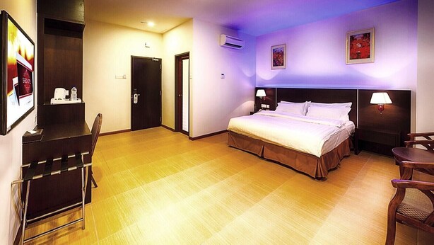 A hotel room with a bed, bedside tables, a desk, a chair, and an air conditioning unit. - E Red Hotel Cosmo (Bukit Mertajam)