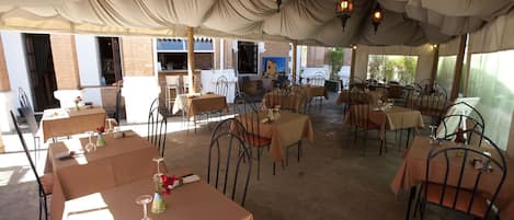 A covered outdoor dining area with tables and chairs, brick walls, and hanging lanterns.