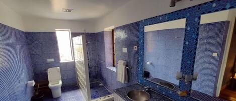 Un baño con mosaicos azules, un espejo grande, un lavamanos y un inodoro.
