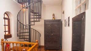 A spiral staircase with black railings and wooden handrails, leading to a landing with a dark wooden cabinet and a small table with a decorative item on top. - Guest House Les 3 Metis (Antananarivo)