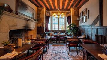 A traditional dining room with wooden beams, a fireplace, and a patterned carpet.