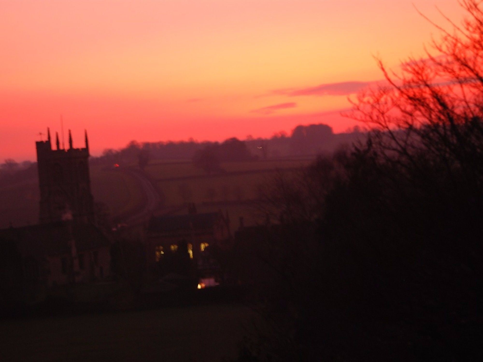 A rural landscape with a church tower and surrounding fields.
