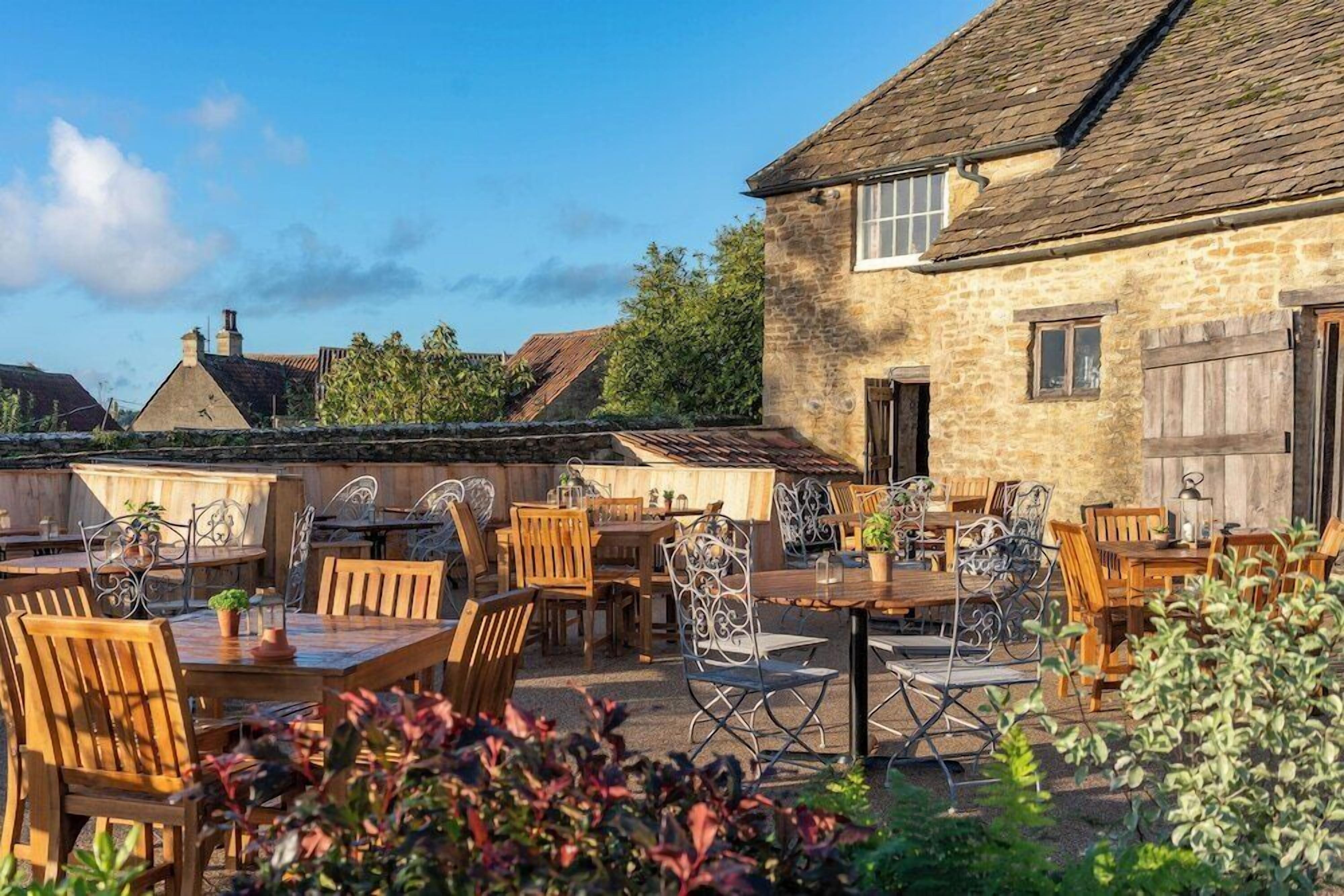 An outdoor dining area with stone buildings, wooden tables, and metal chairs.