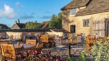 An outdoor dining area with stone buildings, wooden tables, and metal chairs.