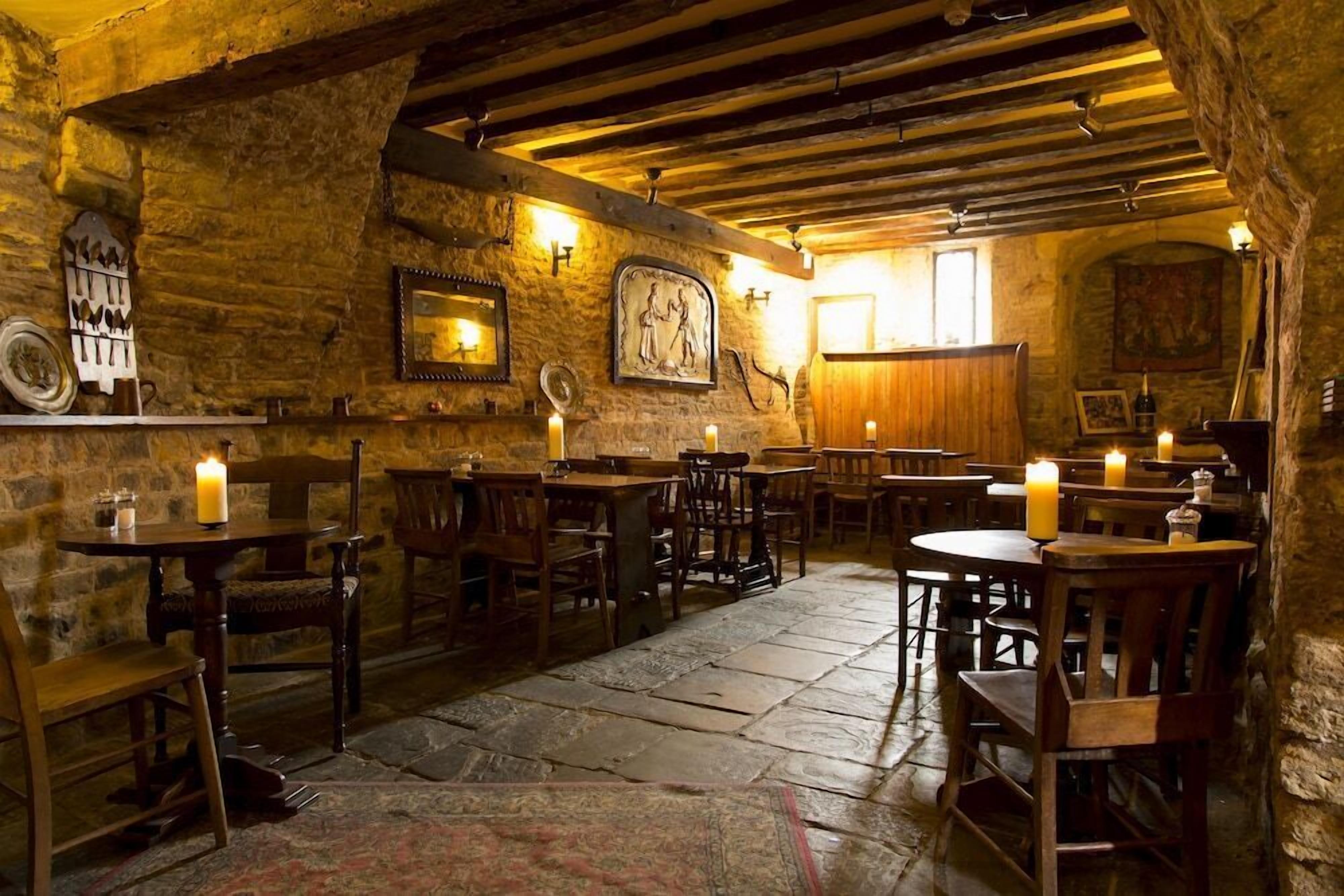Un intérieur rustique avec des murs en pierre, des poutres en bois et des tables éclairées à la bougie.
