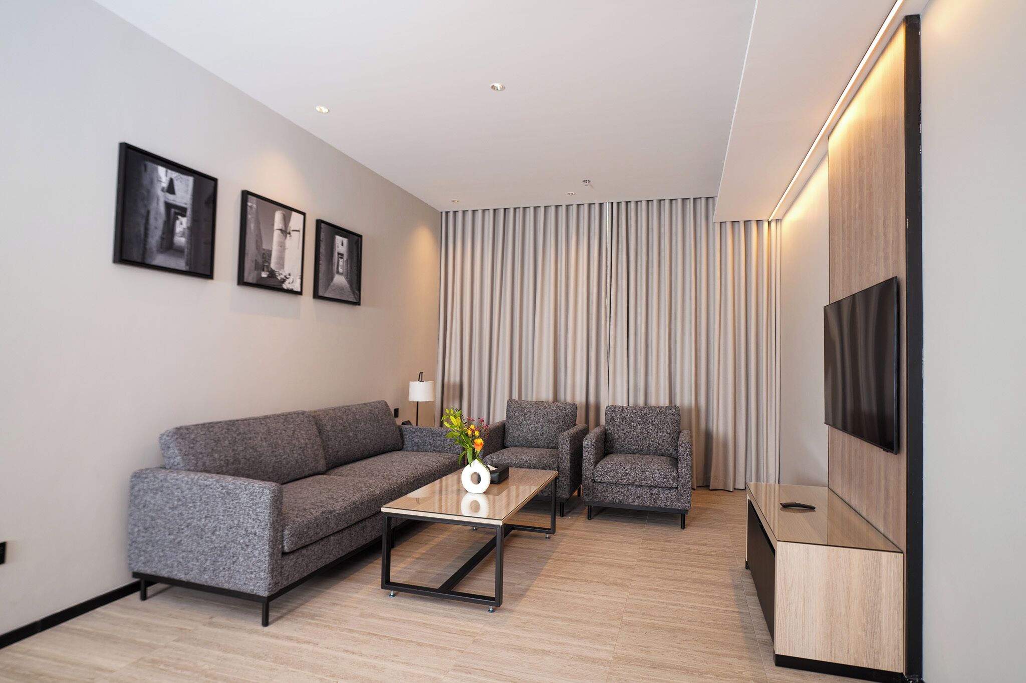 A modern living room with a grey sofa, two armchairs, a coffee table, and a flat-screen TV mounted on the wall.