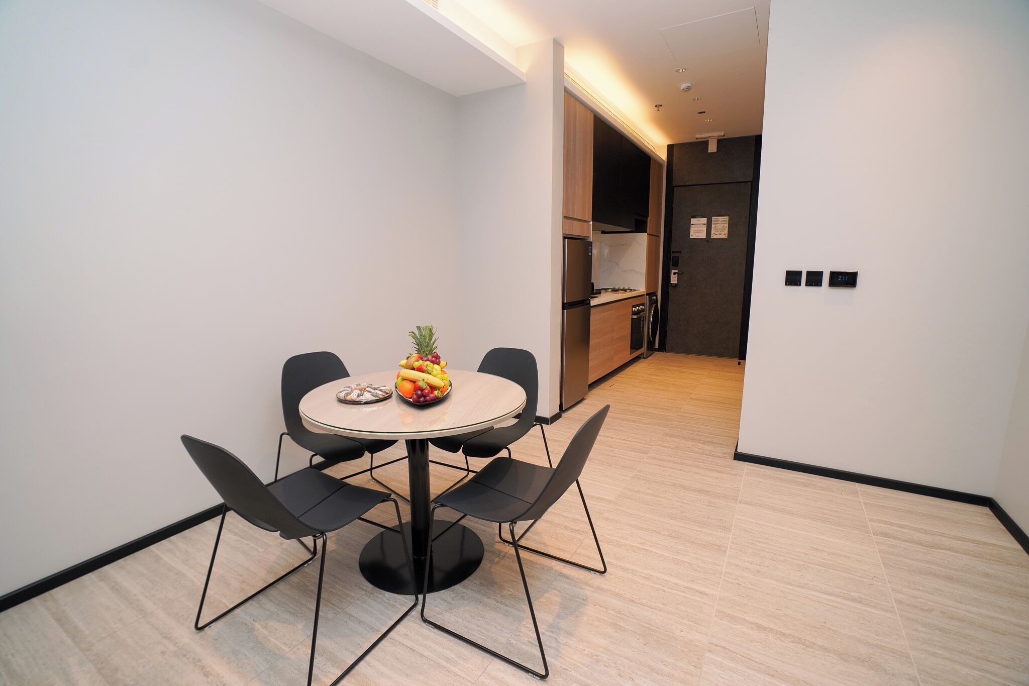 A modern dining area with a round table, four chairs, and a fruit bowl.
