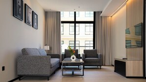 Uma sala de estar moderna com um sofá, duas poltronas, uma mesa de centro e uma TV sobre um armário de madeira.