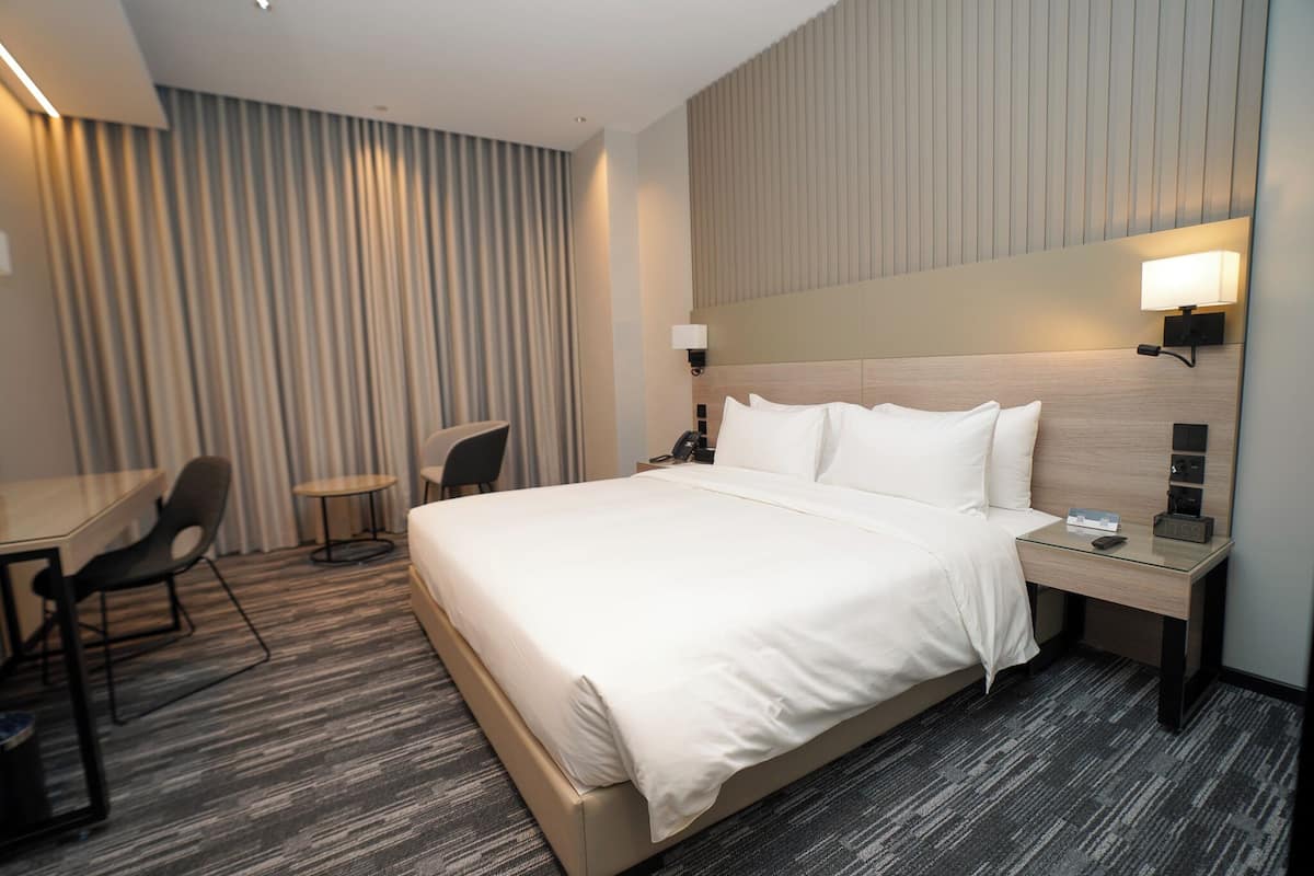 A hotel room with a large bed, a desk, a chair, and a small table.