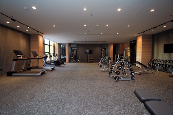 A gym with treadmills, elliptical machines, weight benches, and dumbbells. - Azha Alriyadh Hotel Apartment (Riyadh)