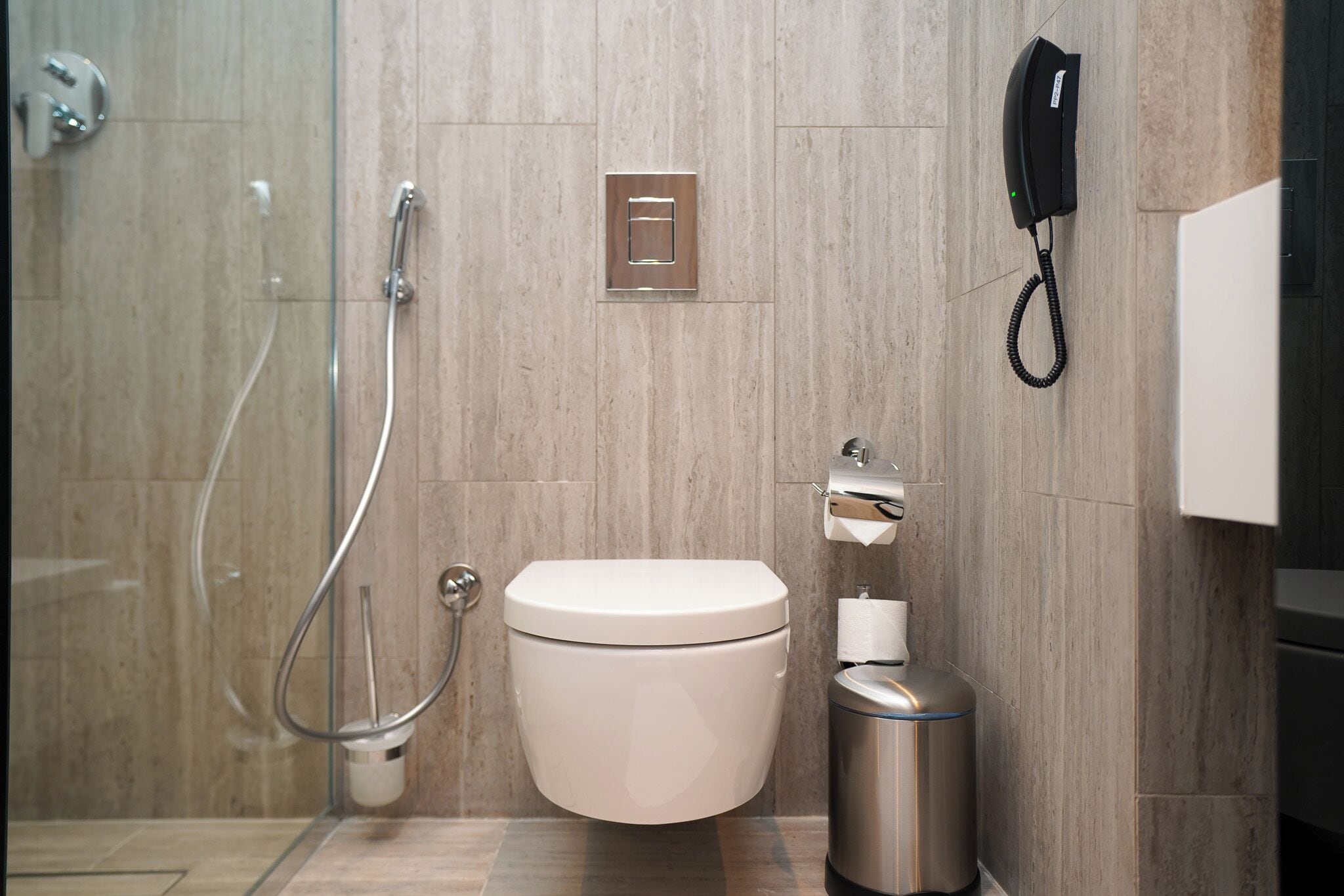 Une salle de bain moderne équipée de toilettes, d’une douche, d’une poubelle et d’un téléphone.