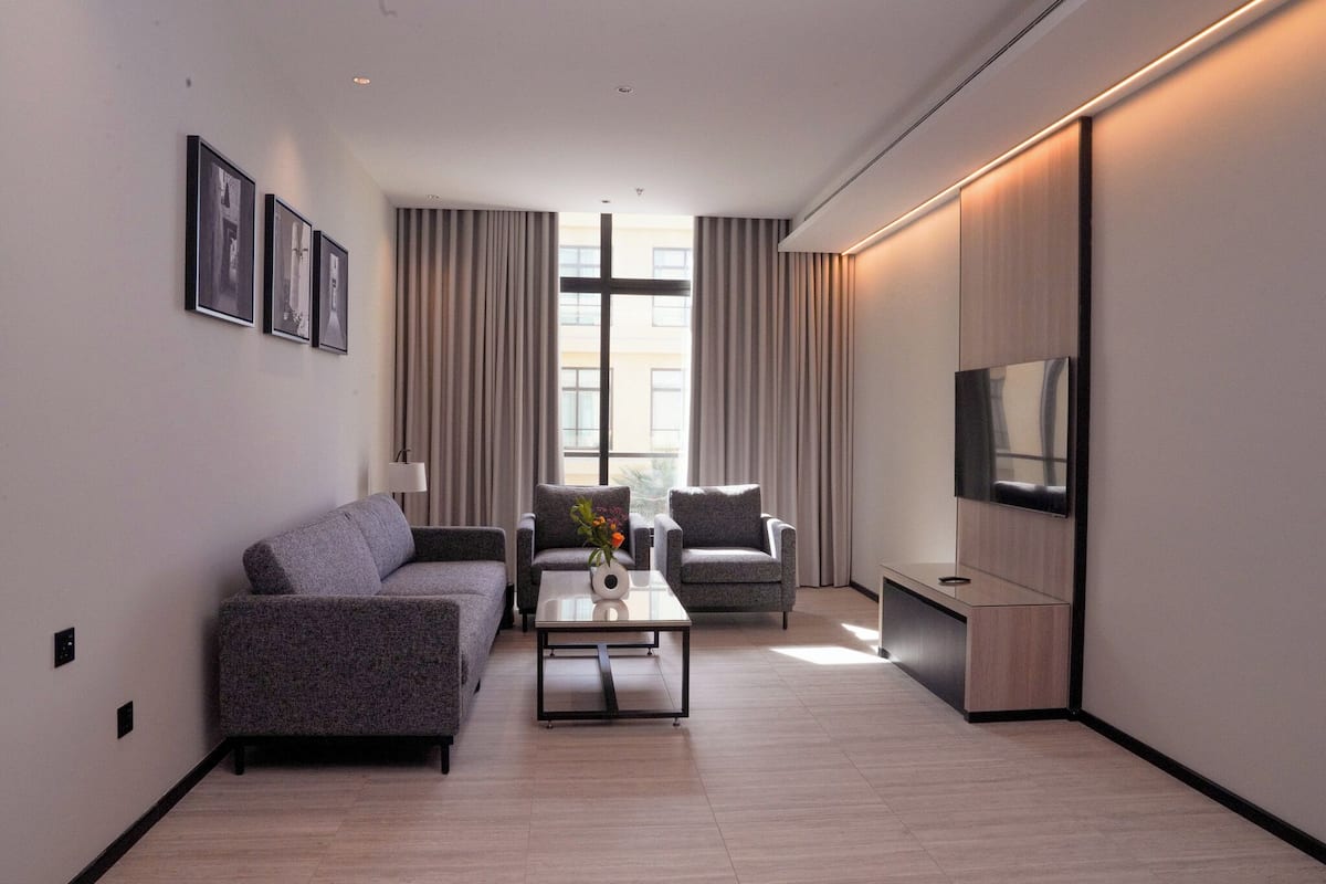 A modern living room with a sofa, armchairs, a coffee table, and a TV.