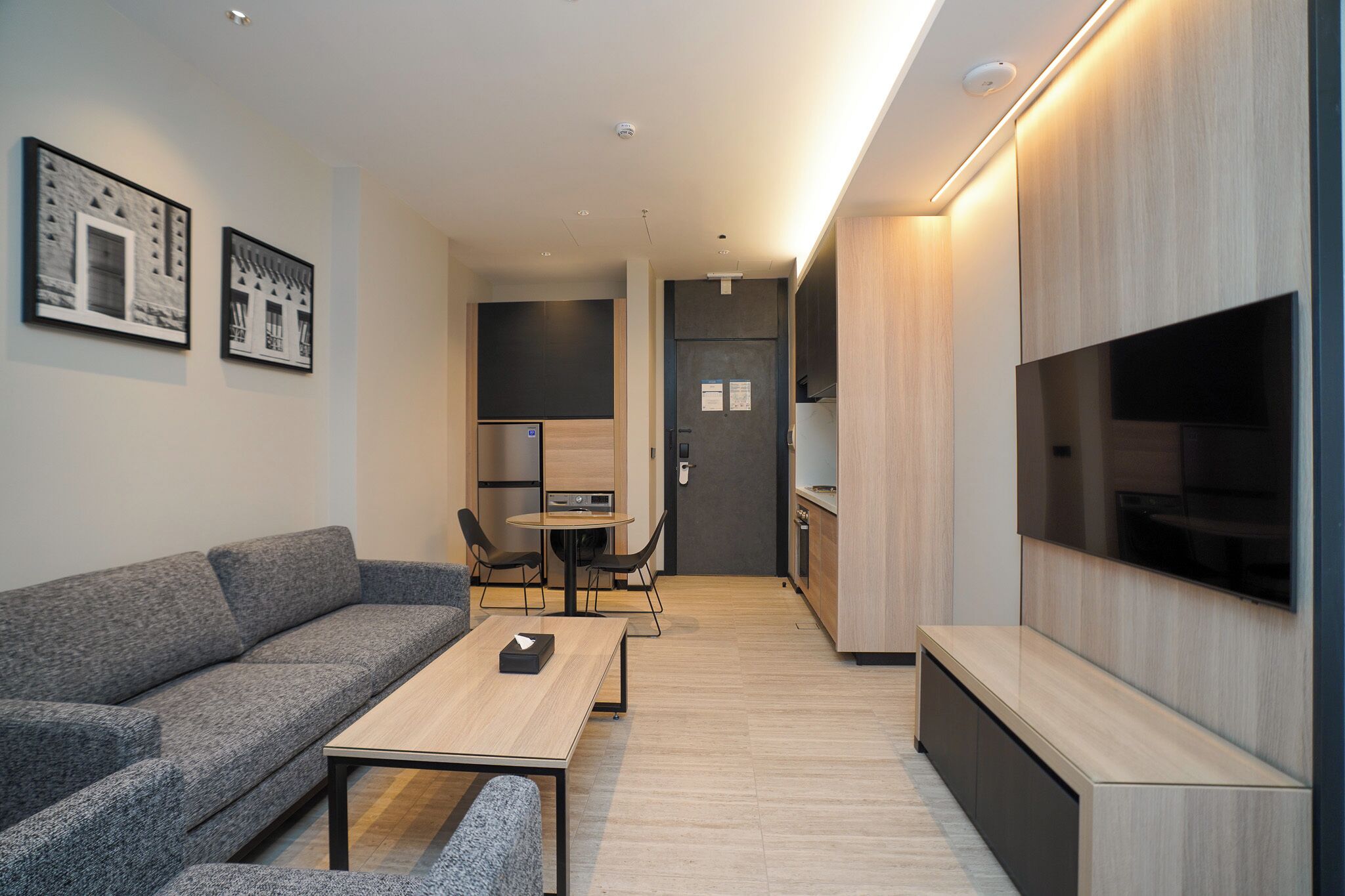 A modern living room with a grey sofa, a wooden coffee table, and a TV mounted on the wall.