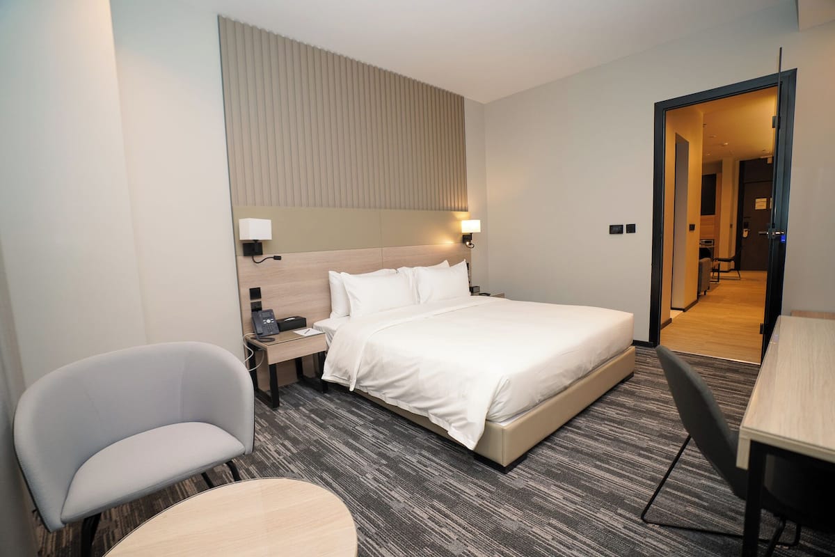 A hotel room with a bed, a desk, a chair, and a lamp.