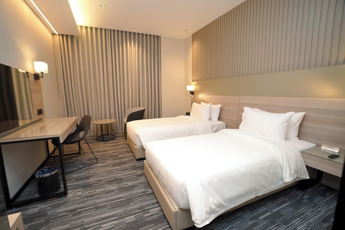 A hotel room with two beds, a desk, a chair, and a small table.