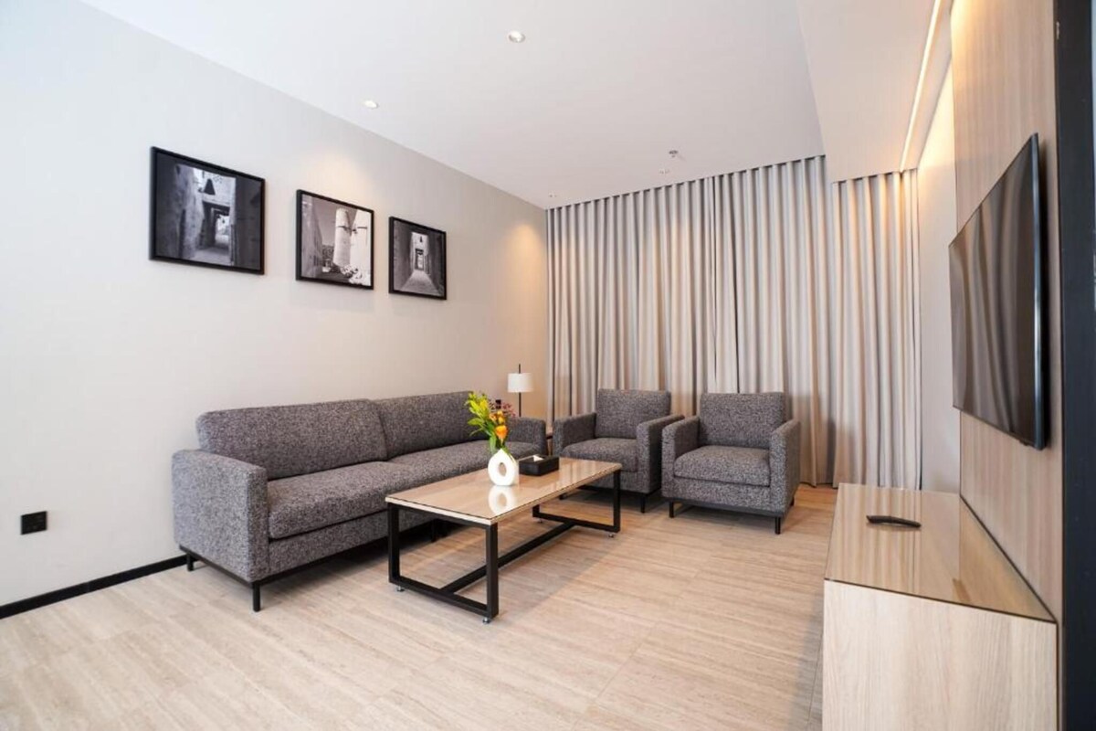 Una sala de estar moderna con un sofá, sillones, una mesa de centro y un televisor de pantalla plana.