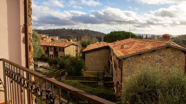 Edificio de piedra con techo de tejas, rodeado de vegetación y otras construcciones en un entorno rural.