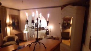 Uma área de refeições com uma mesa de madeira, um candelabro com velas acesas, uma cadeira e um espelho refletindo o ambiente.