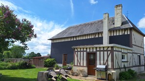 Uma casa com fachada escura e detalhes de madeira aparente, uma chaminé e uma churrasqueira no quintal.