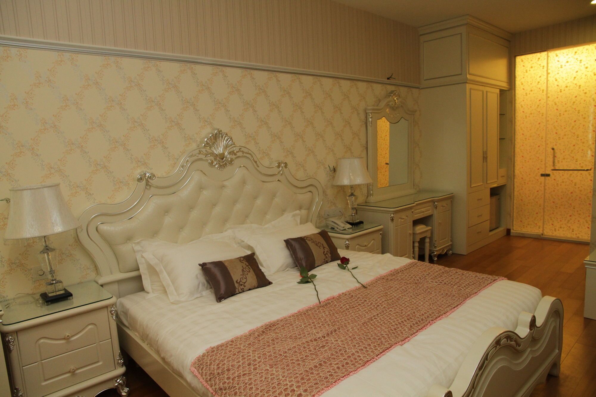 A bedroom with a large bed, two bedside tables with lamps, a dresser, and a wardrobe.