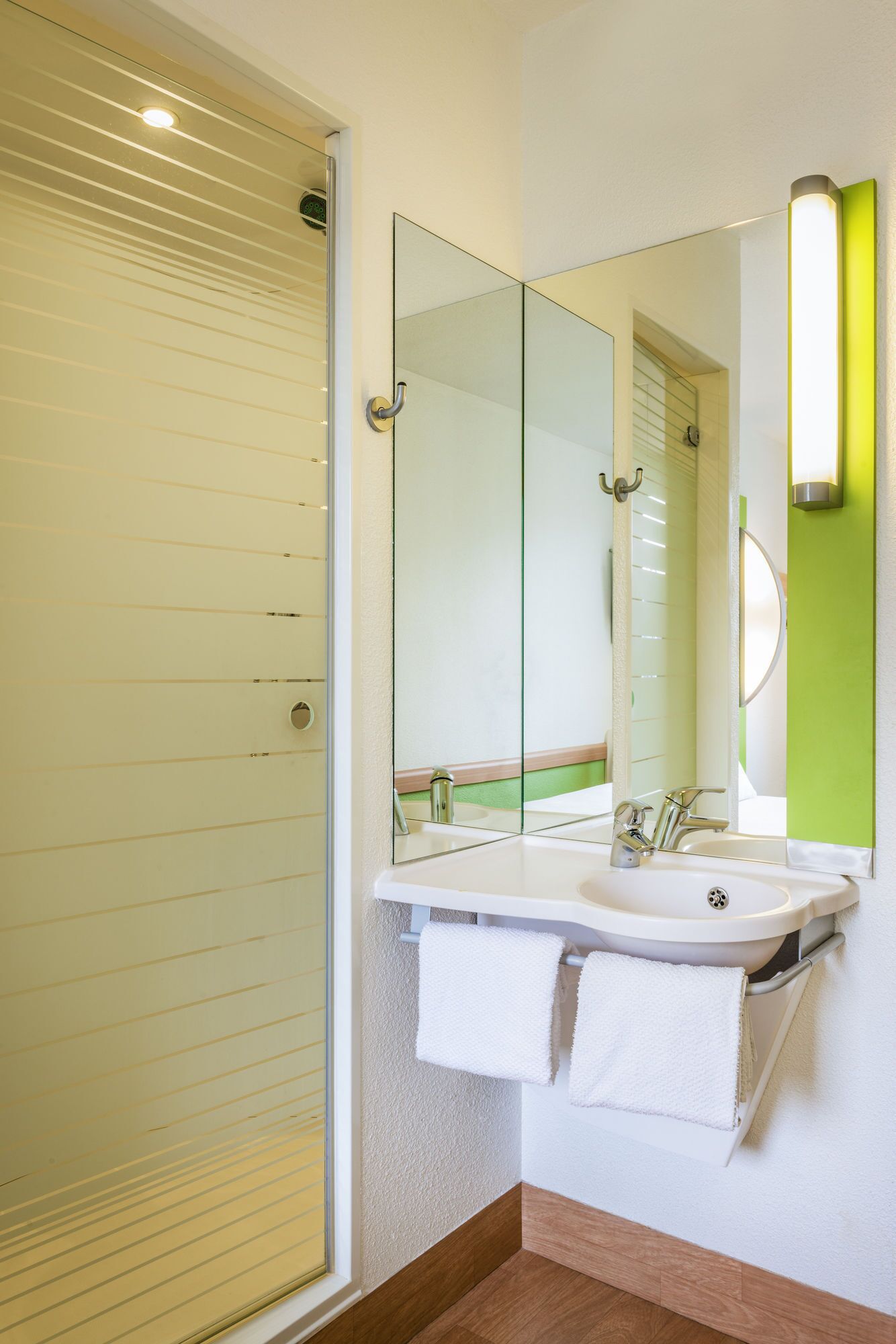 A bathroom with a glass shower door, a white sink with a mirror above it, and a green accent wall.