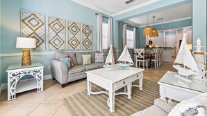 Een woonkamer met een bank, een salontafel en decoratieve zeilboten. Er hangt wanddecoratie en staat een lamp op een bijzettafeltje.