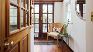 A wooden door with glass panels, a wicker chair with a cushion, a small table with a vase, and a window with a mirror. - The West London House (London)