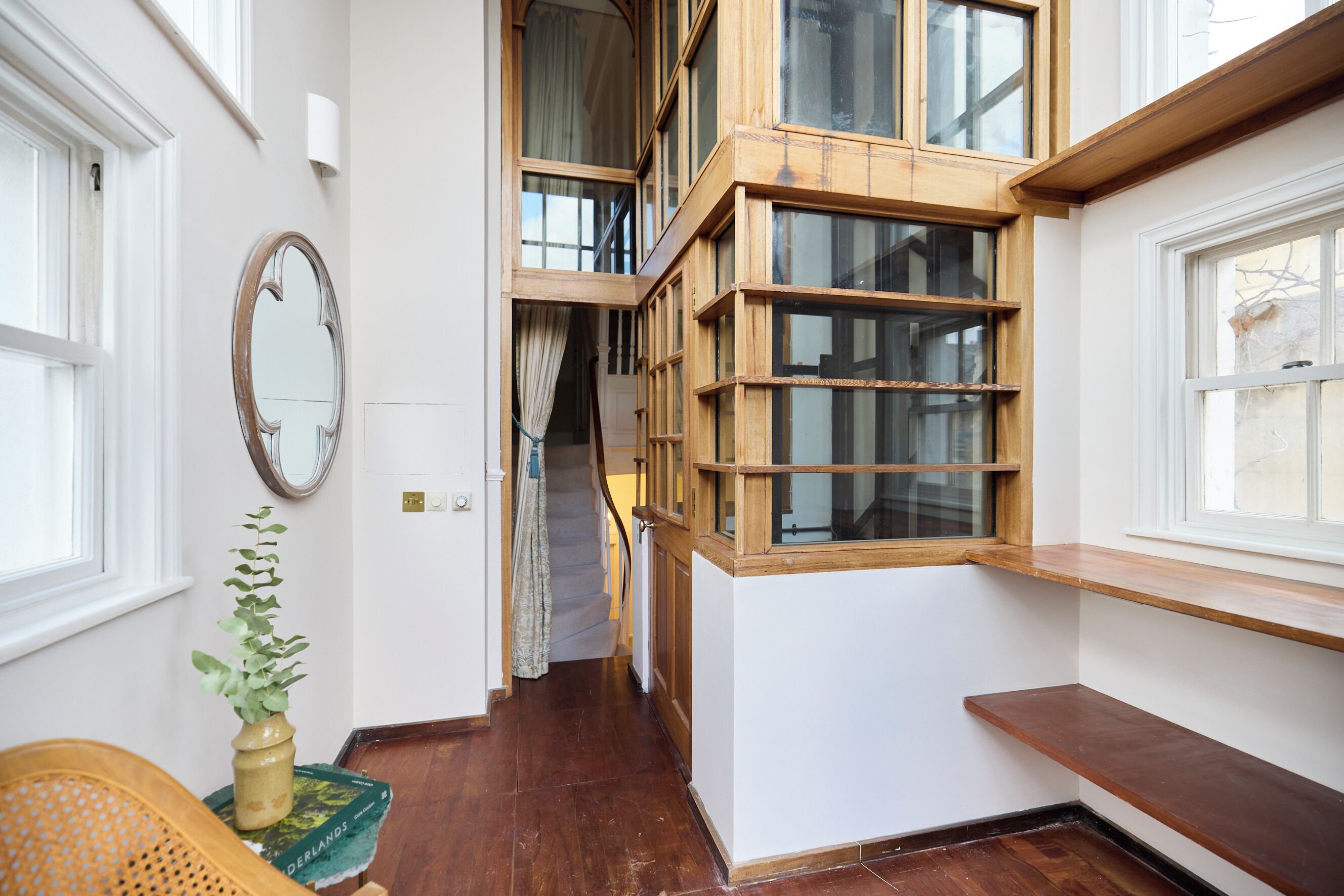 A narrow hallway with wooden shelving, a mirror, and a potted plant.