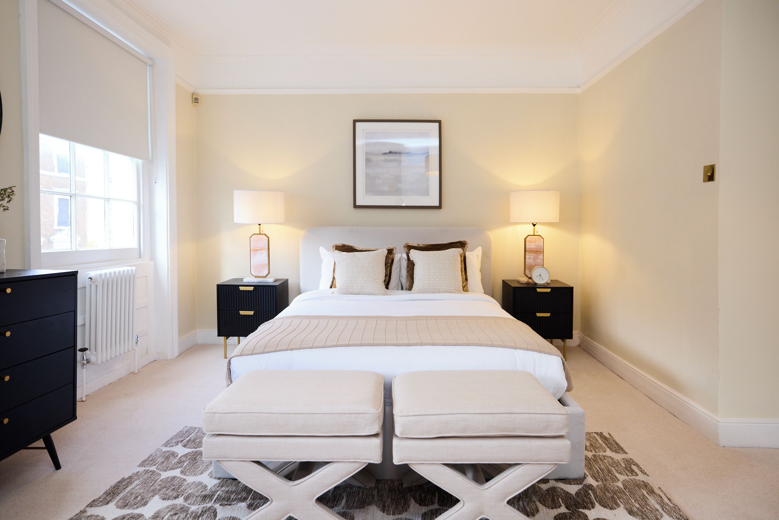 A bedroom with a large bed, two bedside tables with lamps, a dresser, and a radiator.
