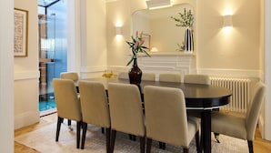 A dining room with a round table, six chairs, a vase with flowers, a fireplace, and a large mirror on the wall. - The West London House (London)