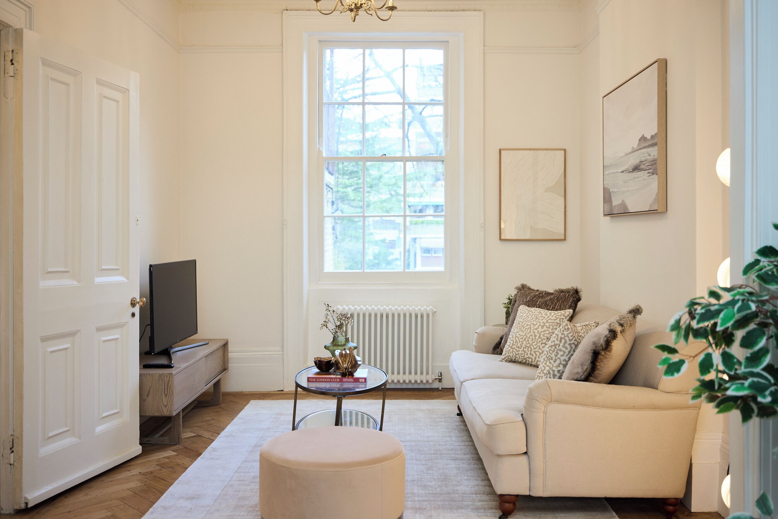 Una sala de estar con un sofá, un reposapiés y un televisor sobre un mueble.