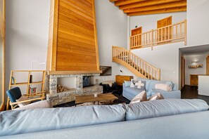 A cozy living room with a stone fireplace, a blue sofa, a wooden staircase, and a bookshelf. - Crevasse 07 - Elegant duplex & private sauna (Haute-Nendaz)
