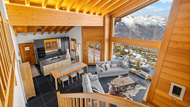 A spacious wooden interior with a kitchen, dining area, and seating area overlooking a snowy mountain landscape. - Crevasse 07 - Elegant duplex & private sauna (Haute-Nendaz)