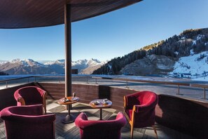 Una terraza con sillas y mesas rojas, con vistas a un paisaje montañoso nevado.