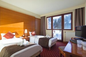 A hotel room with two beds, a TV, a desk, and a window with a view of trees and snow.