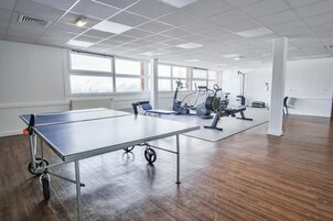 Um quarto espaçoso com mesa de pingue-pongue, equipamentos de ginástica e janelas grandes.