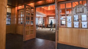 A wooden interior with a restaurant sign, glass display cases, and a person walking. - Hotel La Plagne Le Terra Nova - Winter (La Plagne-Tarentaise)