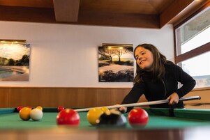 A person playing pool in a room with wooden ceiling beams and two framed pictures on the wall.