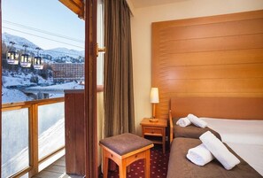 A hotel room with a bed, a small table, a nightstand, a lamp, and a view of a snowy landscape with a train.