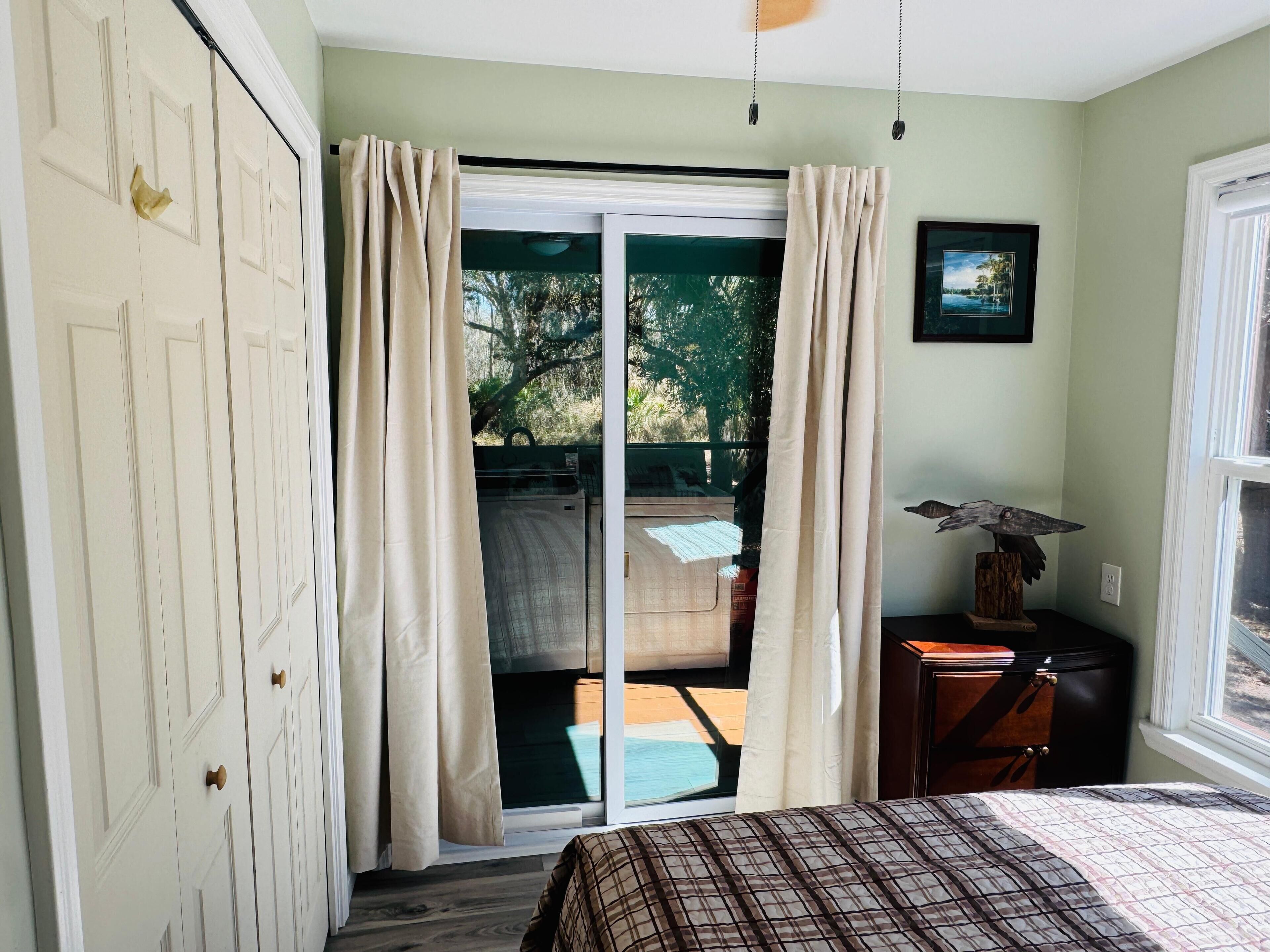 A bedroom with a bed, a sliding glass door leading to a balcony, a small table with a lamp, and a framed picture on the wall.