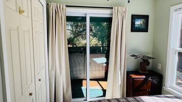 A bedroom with a bed, a sliding glass door leading to a balcony, a small table with a lamp, and a framed picture on the wall.