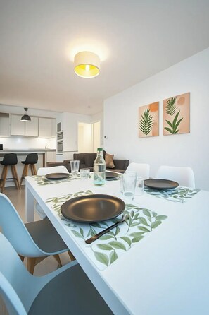 A modern dining area with a white table set for four, featuring a leaf-patterned tablecloth. - Escale Horizon - 2 bedrooms near Orly (Athis-Mons)