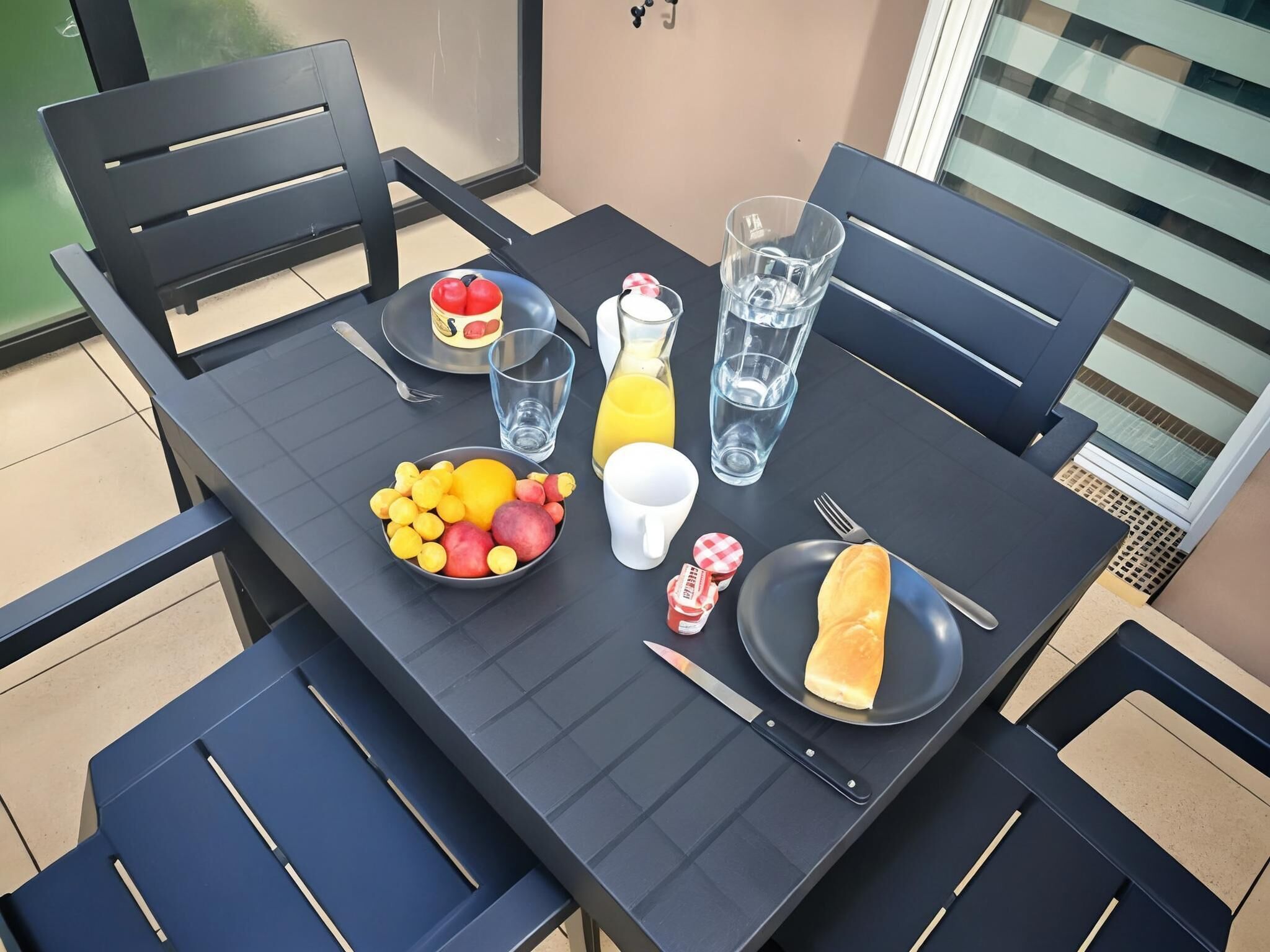 Et bord dækket med en skål frugt, et glas appelsinjuice, et glas vand, en tallerken med et stykke brød og en kniv.