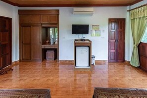 A room with wooden flooring, a television mounted on the wall, a small refrigerator, and a cabinet. - Khaosok Rainforest Resort (Phanom)